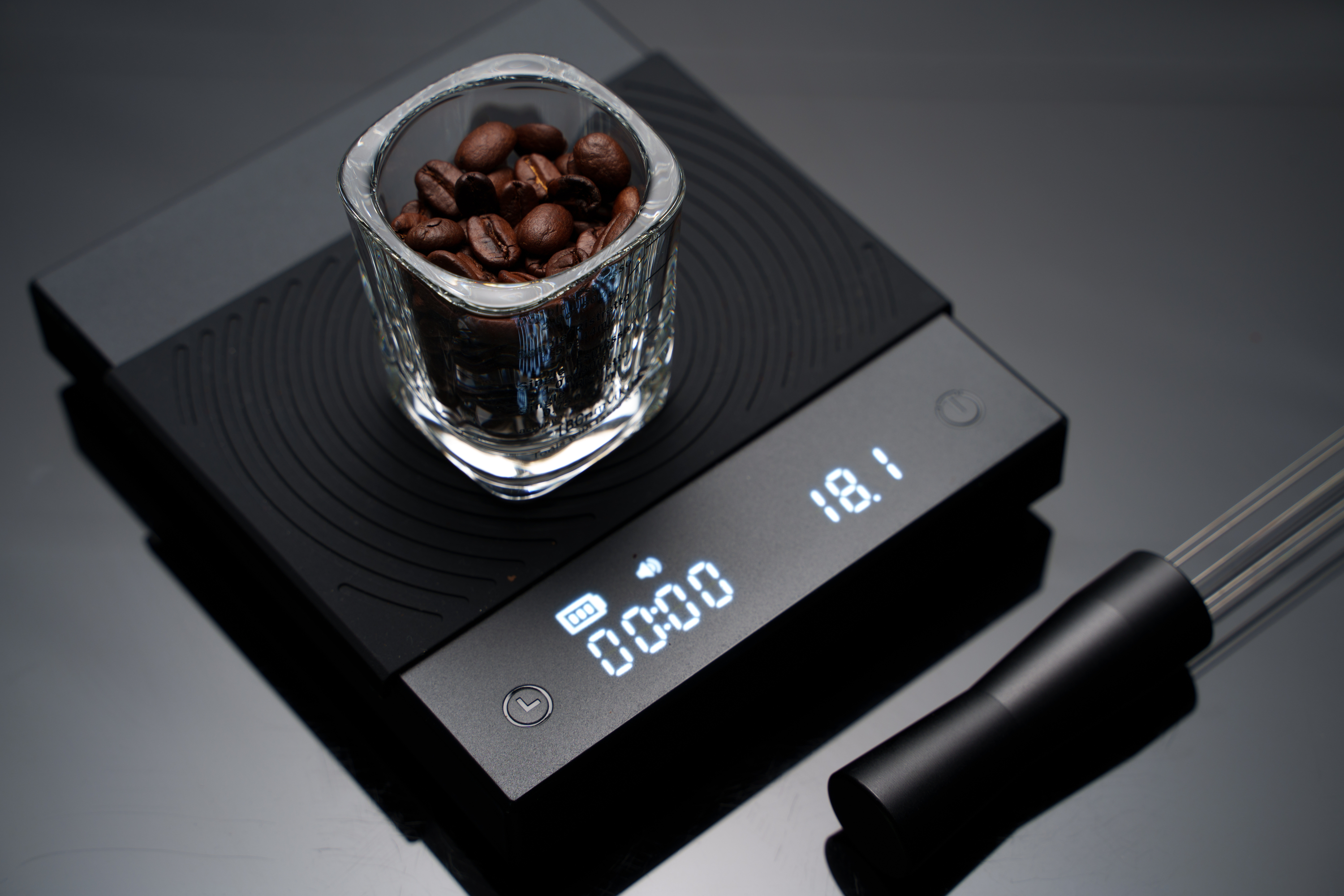 Un verre à expresso rempli de grains de café placé sur des écailles de café noir et un plan de travail sombre