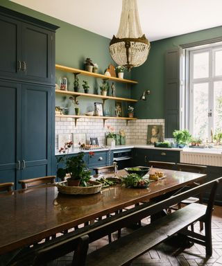 navy devol kitchen with green walls and a long kitchen table with a large chandelier