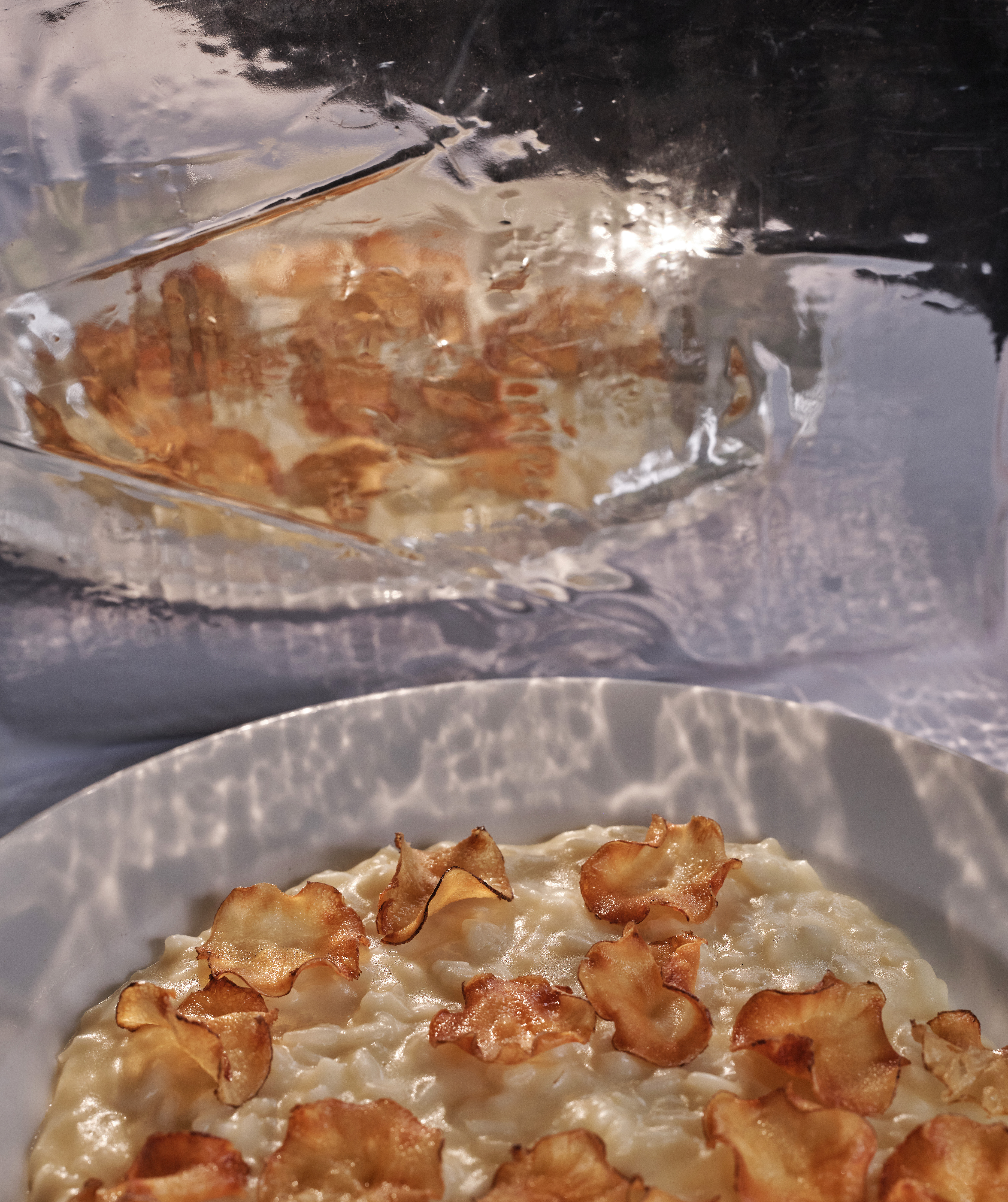 Two theatrically plated dishes, one filled with creamy risotto, topped with crunchy, paper-thin pancetta, the other, showing a scallop in its shell.