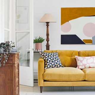 White living room with yellow sofa in front of oversized artwork