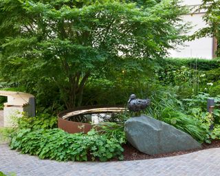 A round water feature in a flowerbed in a rock garden with curved pathway.