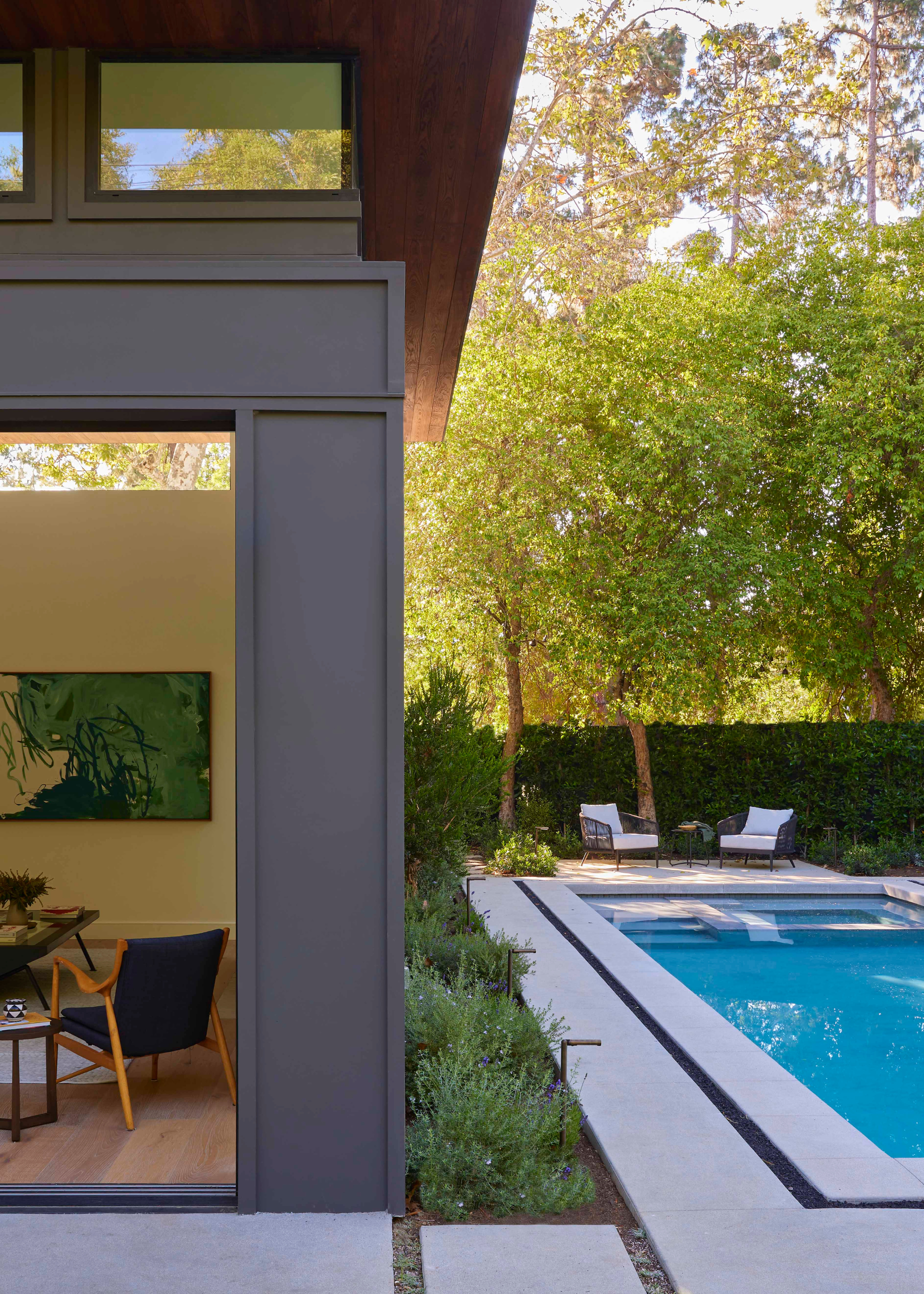 A backyard with manicured hedges. There is also a pool in the backyard with outdoor seating