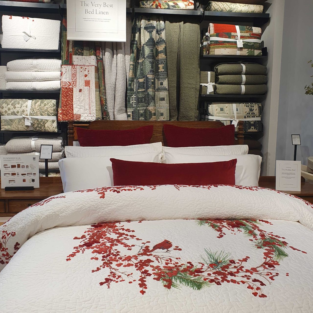 A bed dressed with a Christmas quilt and dark red velvet cushions from Pottery Barn at the brand's London store