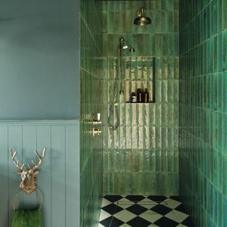 a dark green bathroom with wood panelling and vertically hung metro wall tiles, brass fixtures and monochrome tiled flooring