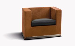 White background, tan coloured suitcase design armchair, with a dark brown seat cushion, silver metal trim around the bottom of the chair