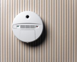 A wall-mounted carbon monoxide alarm on striped wallpaper