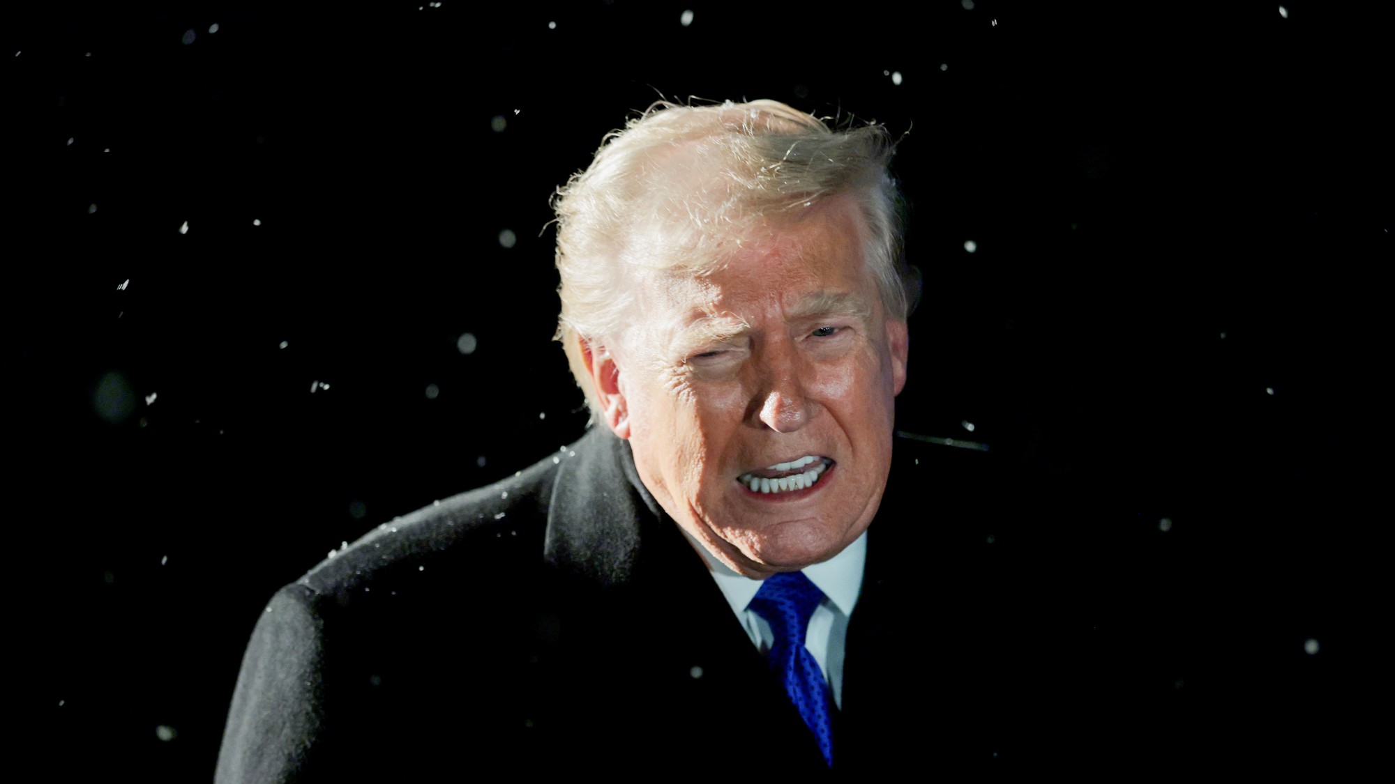 President Donald Trump speaks to reporters at night, with snowflakes falling