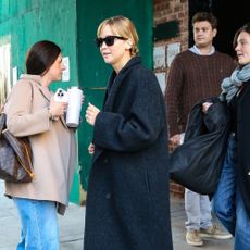 Jennifer Lawrence walks outside wearing a grey wool coat, blue jeans and rounded-toe flat shoes.