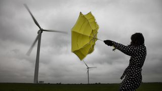 A woman's yellow umbrella is turned inside out as she stands near wind turbines