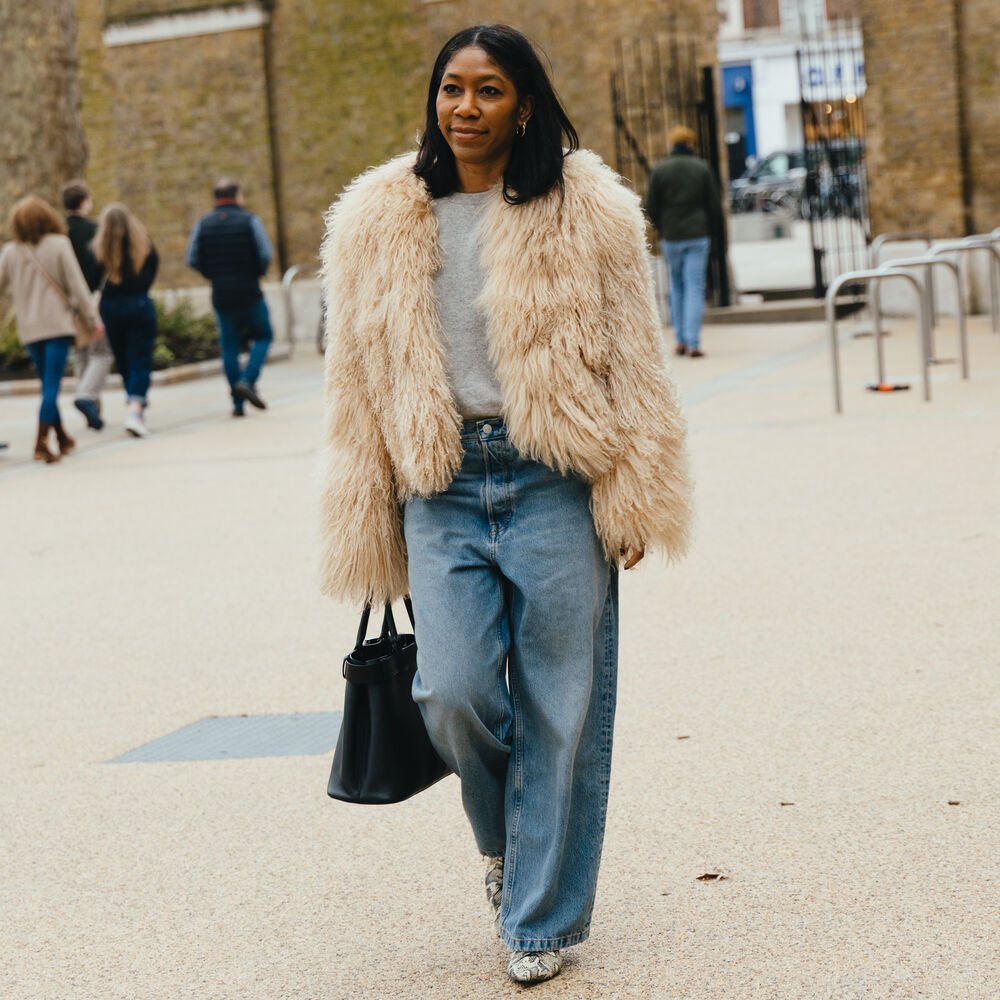 woman wears jeans, gray shirt, heels, black bag, and cream faux fur jacket 