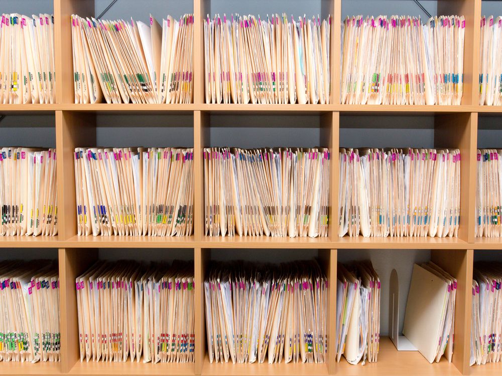 Stacks of paper patient records stored on a doctor&amp;#039;s shelf