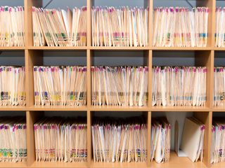Stacks of paper patient records stored on a doctor's shelf