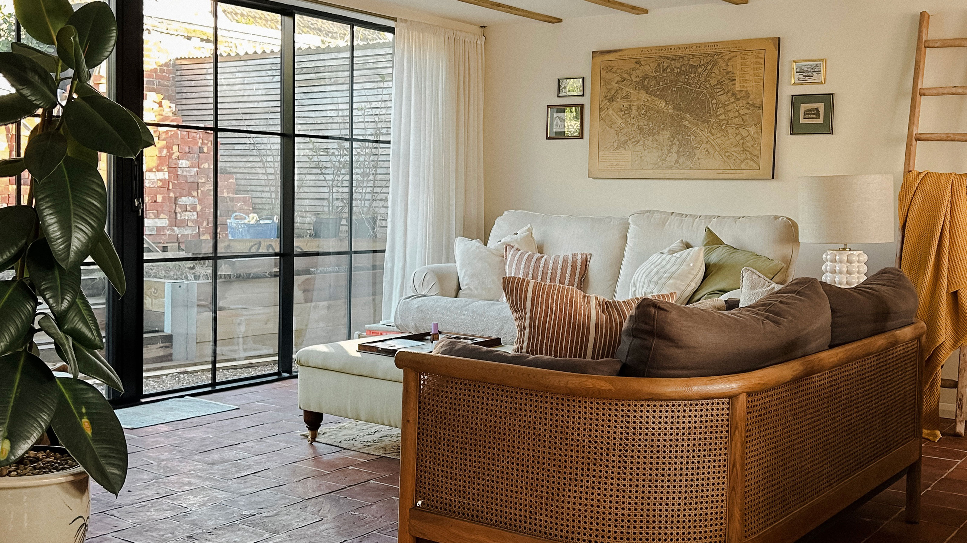 Living room with crittall style doors, terracotta tiled floor, cane backed sofa and map as artwork on wall