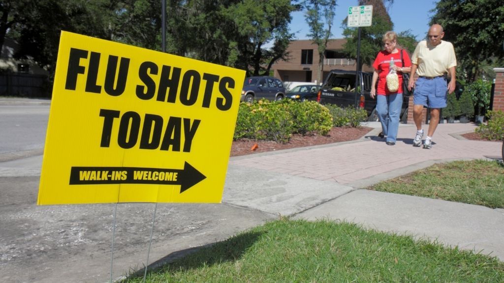 Yard sign that read &quot;flu shots today, walk-ins welcome.&quot; two people can be seen walking in the background 