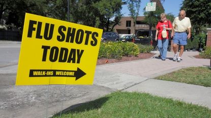 Yard sign that read "flu shots today, walk-ins welcome." two people can be seen walking in the background