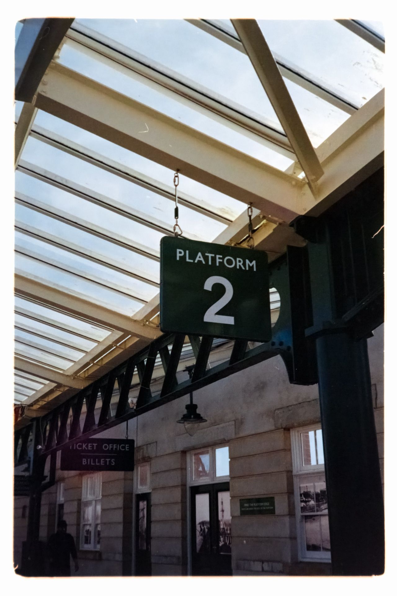 Scanned film image of a railway station sign reading &ldquo;Platform 2&rdquo; beneath a glass canopy.
