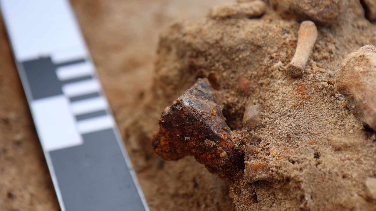 Close up image of iron padlock attached to the foot of a child's skeletal remains with scale.
