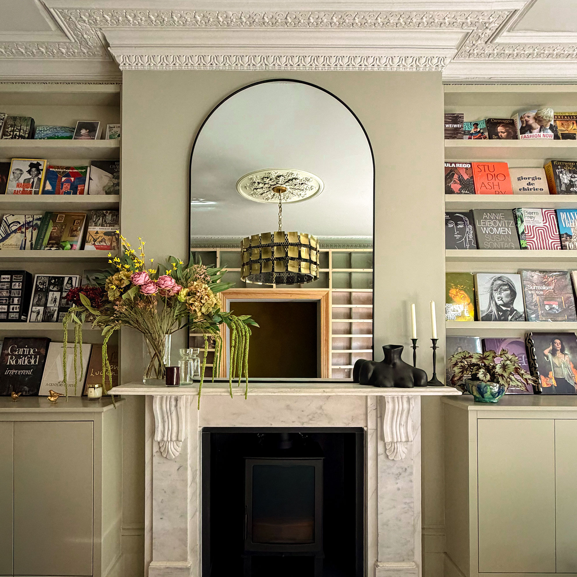Pale green living room with marble fireplace, with large arched mirror above and built in book shelves on either side