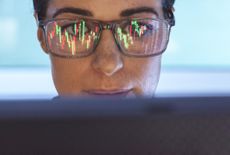 woman looking at a computer screen that's reflecting stock charts in her glasses