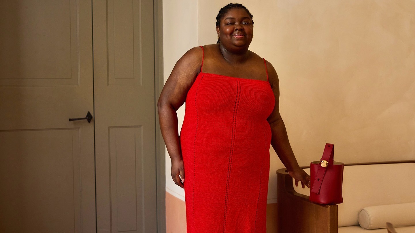 Woman wears a red pointelle column dress and black pumps. 