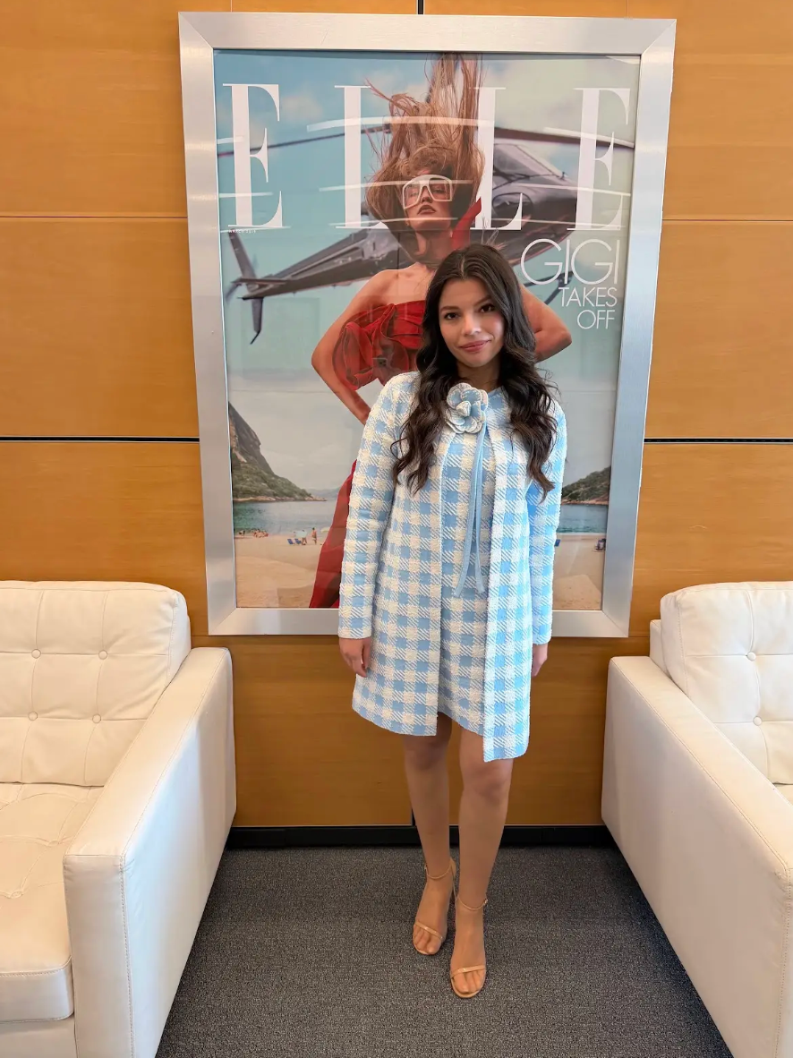 Author Alex Aster poses in the offices of Elle Magazine wearing a matching baby blue and white gingham dress and jacket set.