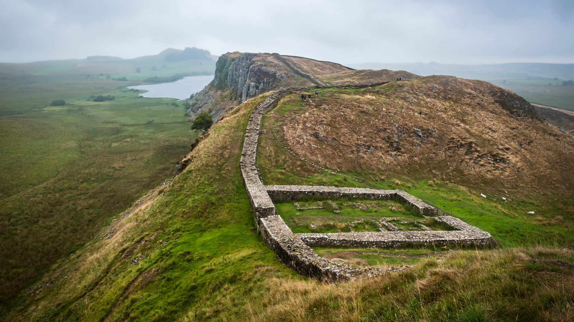 low wall on a hill stretching towards a cliff and the sea on an overcast day