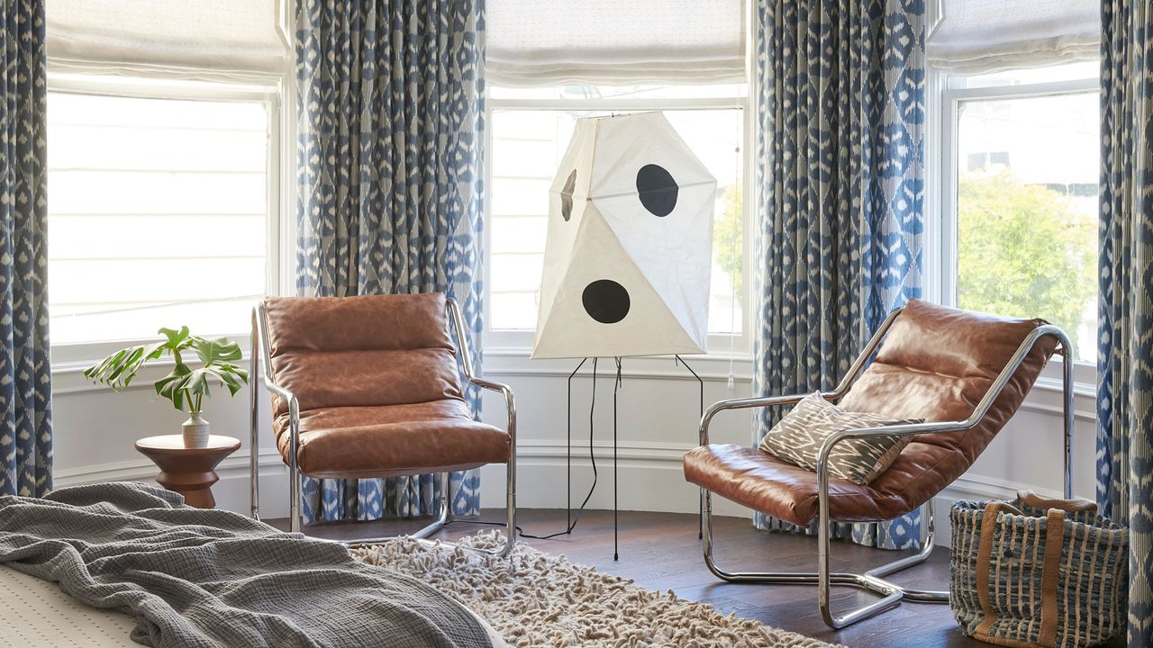 bedroom with lots of natural light, curtains and blackouts, two brown leather armchairs and a statement floor lamp