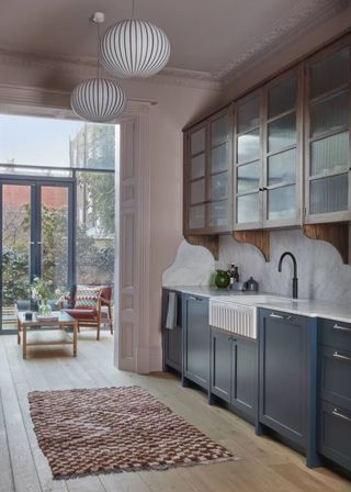 Blue base kitchen cabinet unites with glass cabinets above. A rug sits in the middle of the kitchen and light pendants hang above.