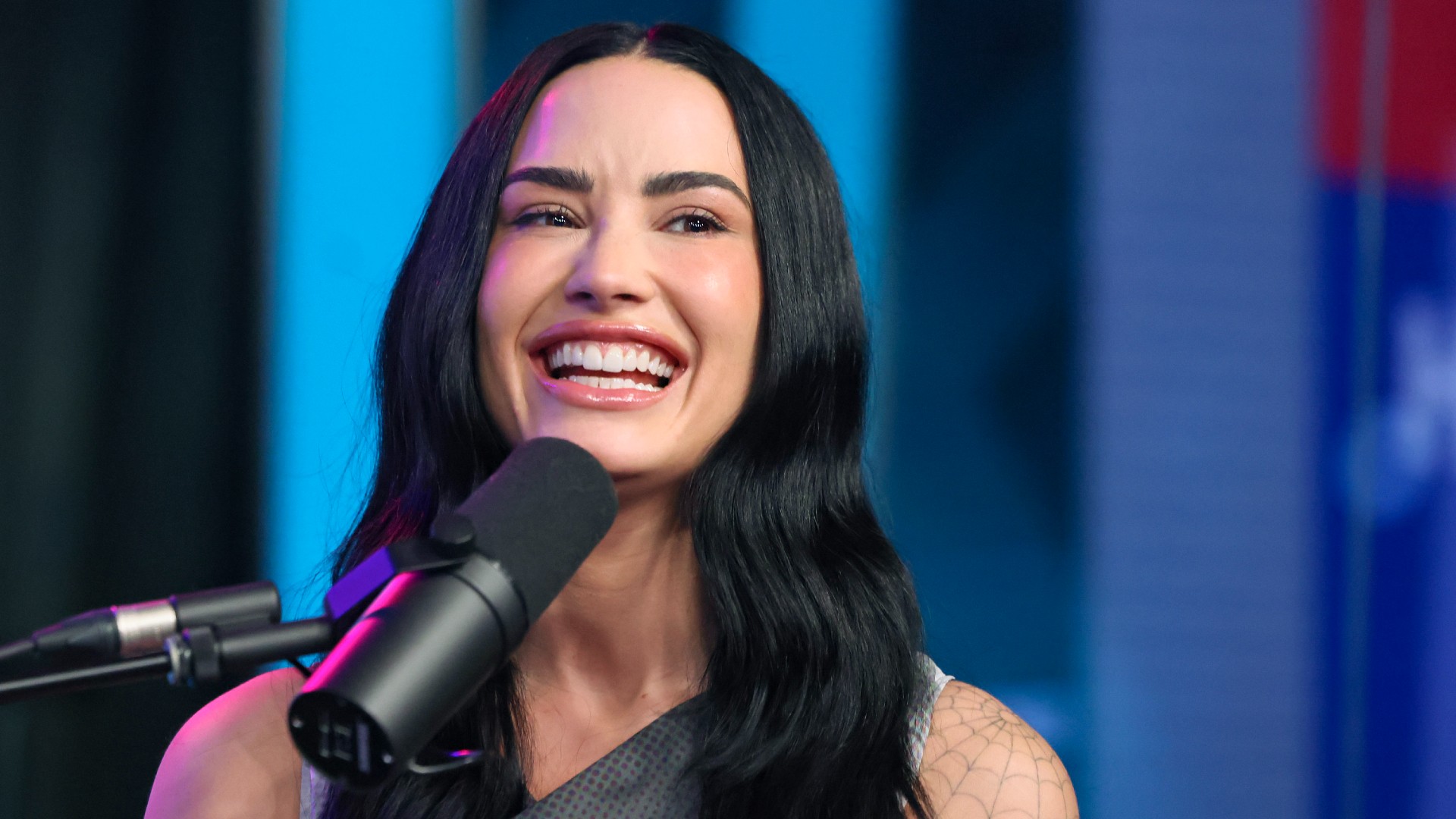 a white woman with long, dark hair laughing in front of microphone while speaking on a radio show