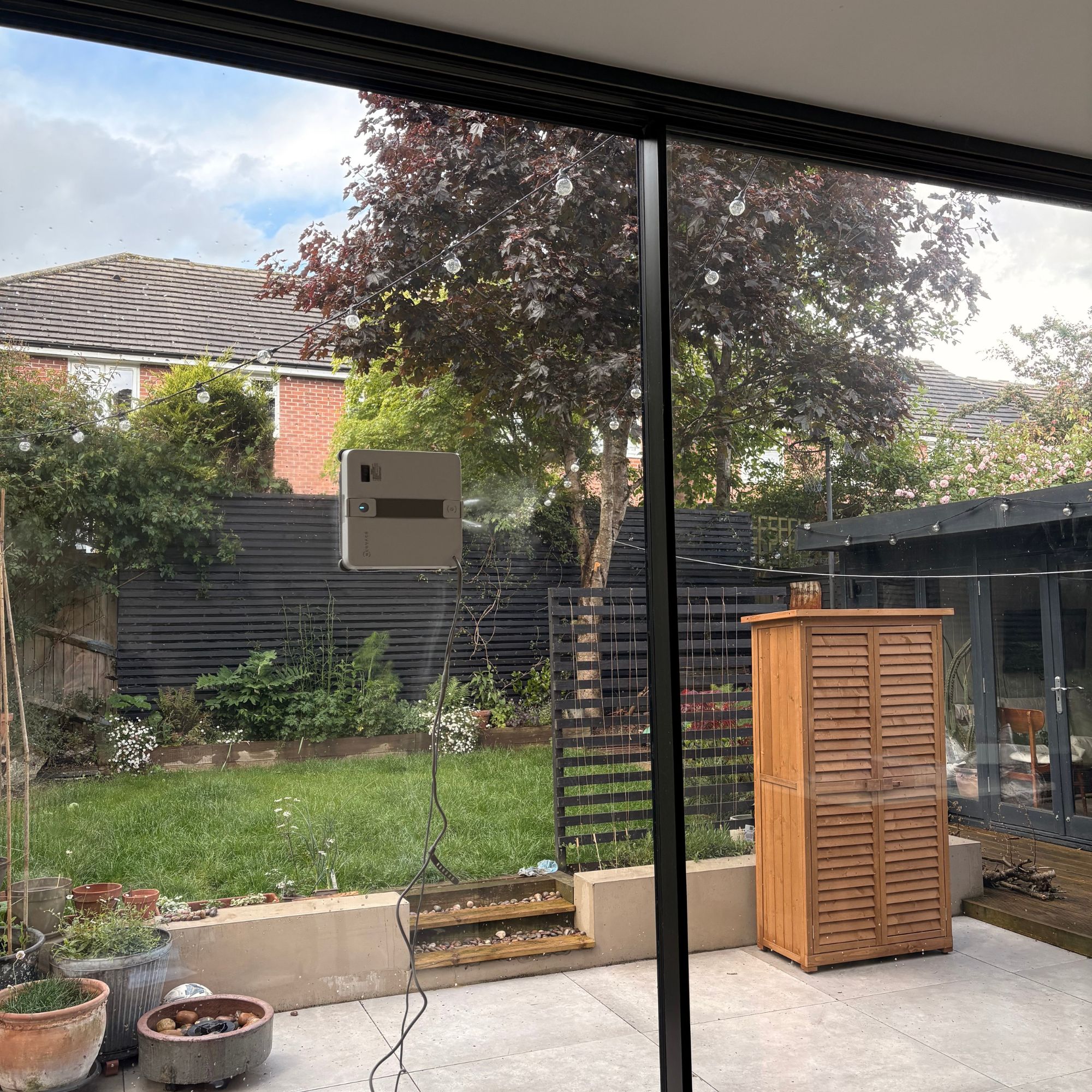 Robot window cleaner on large floor-to-ceiling glass doors, looking out onto a garden beyond