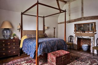 traditional bedroom with wooden four poster bed and chest of drawers and marble fireplace and wooden mantelpiece
