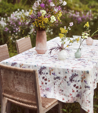 table laid in a garden with a floral tablecloth and vases with flowers on top