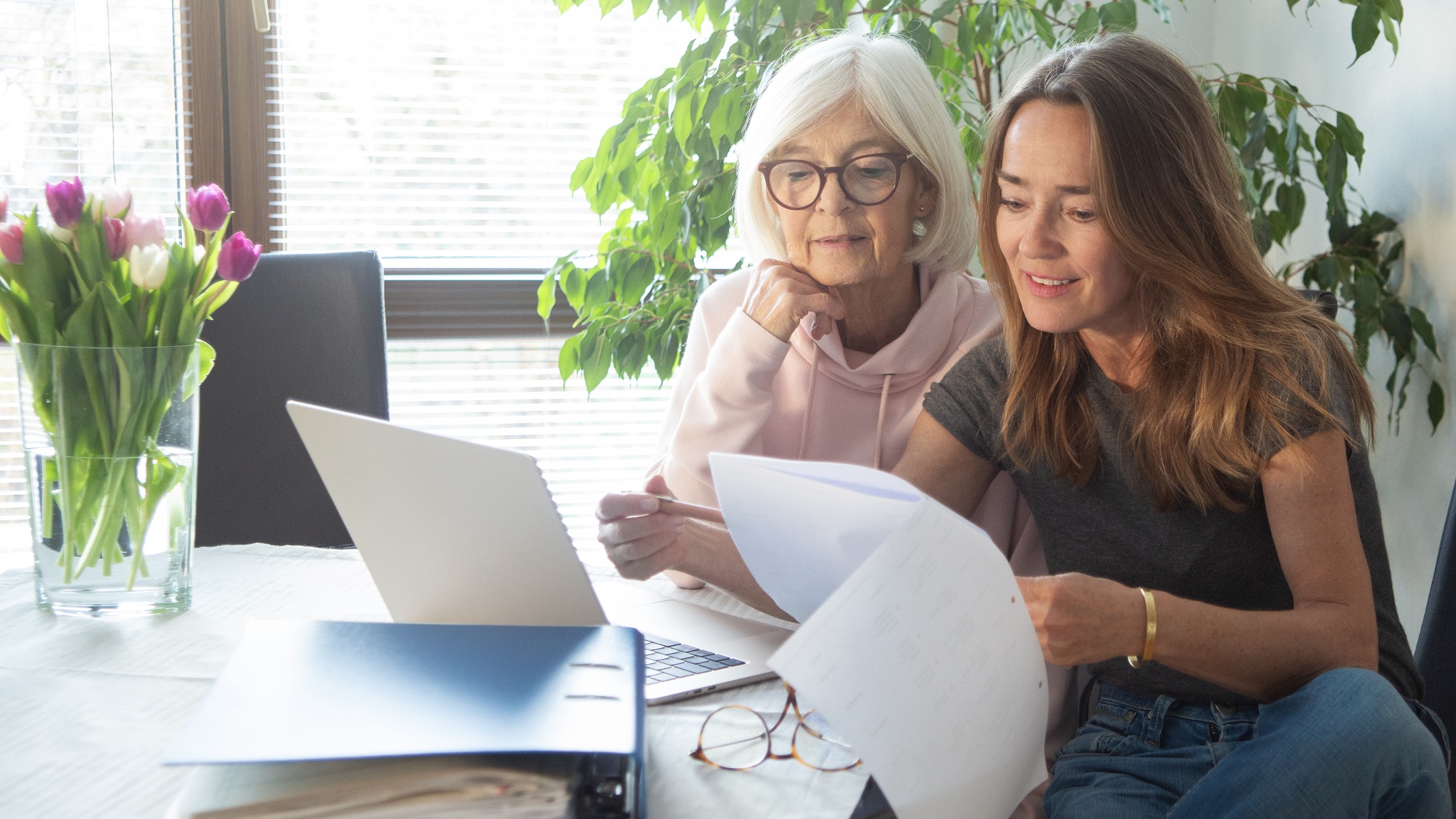 An older woman and her adult daughter look at paperwork together at the kitchen table.