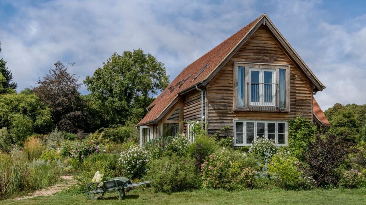 Exterior of a timber clad, oak framed house with lawn and flower beds. A new build oak framed two bedroom house in the New Forest in Hampshire, home of Elizabeth and Derek Sandeman