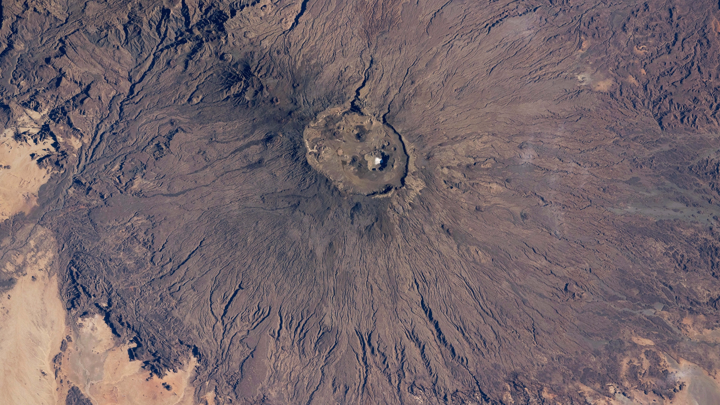 Satellite photo of a volcano in the Sahara desert with a bright-white spot at its summit