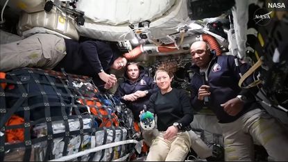 Four people wearing black long sleeve shirts and tan pants float in a small room