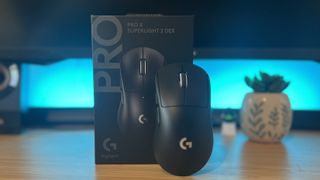 Logitech G Pro X Superlight 2 DEX gaming mouse leaning against packaging on a wooden desk with blue lighting