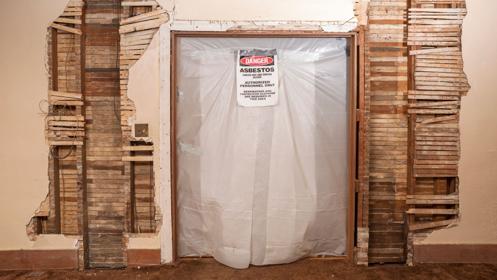 part exposed lath and plaster walls with opening into another room taped over with plastic and asbestos warning sign