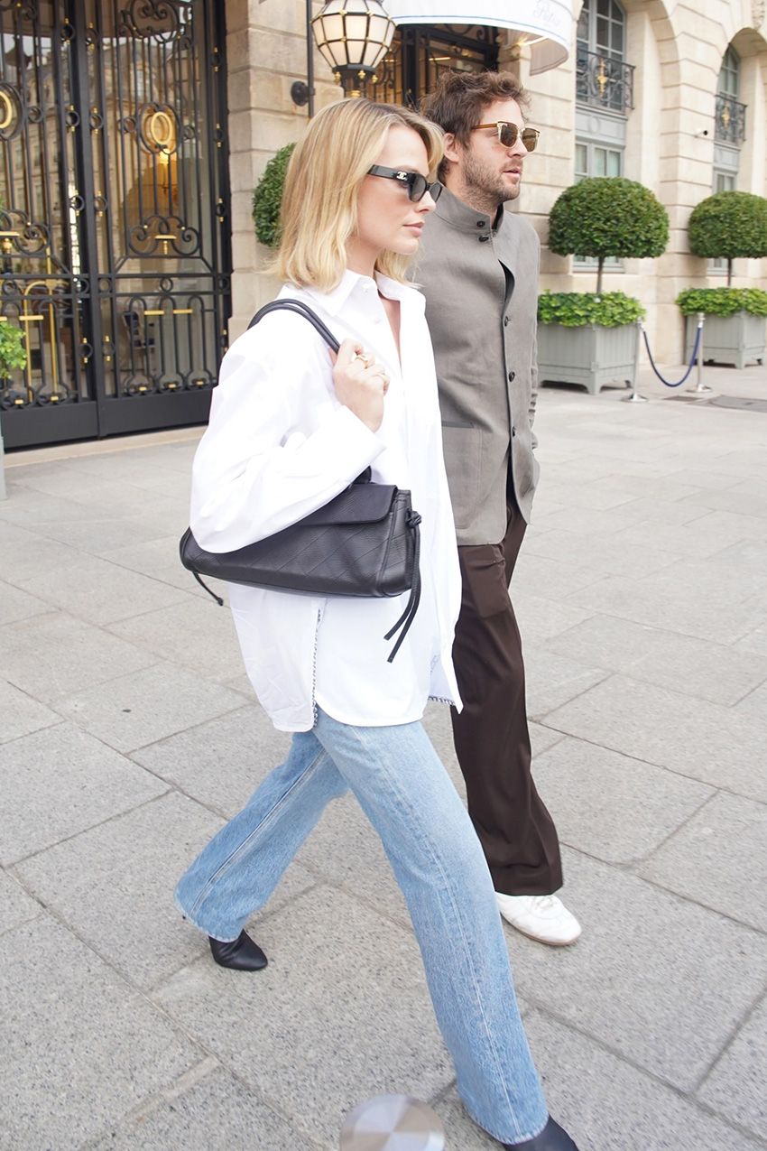 Margot Robbie wearing a white button-down, light-wash jeans, and black pumps, leaving The Ritz in Paris with husband Tom Ackerley