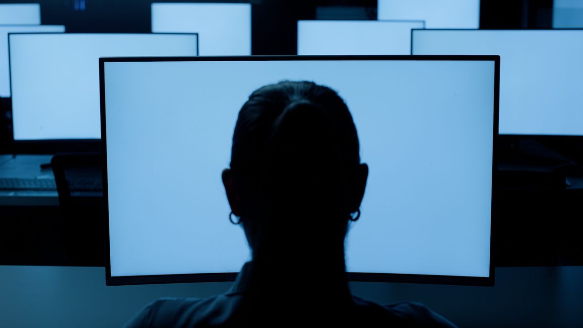 The silhouette of a head outlined against many blue computer screens