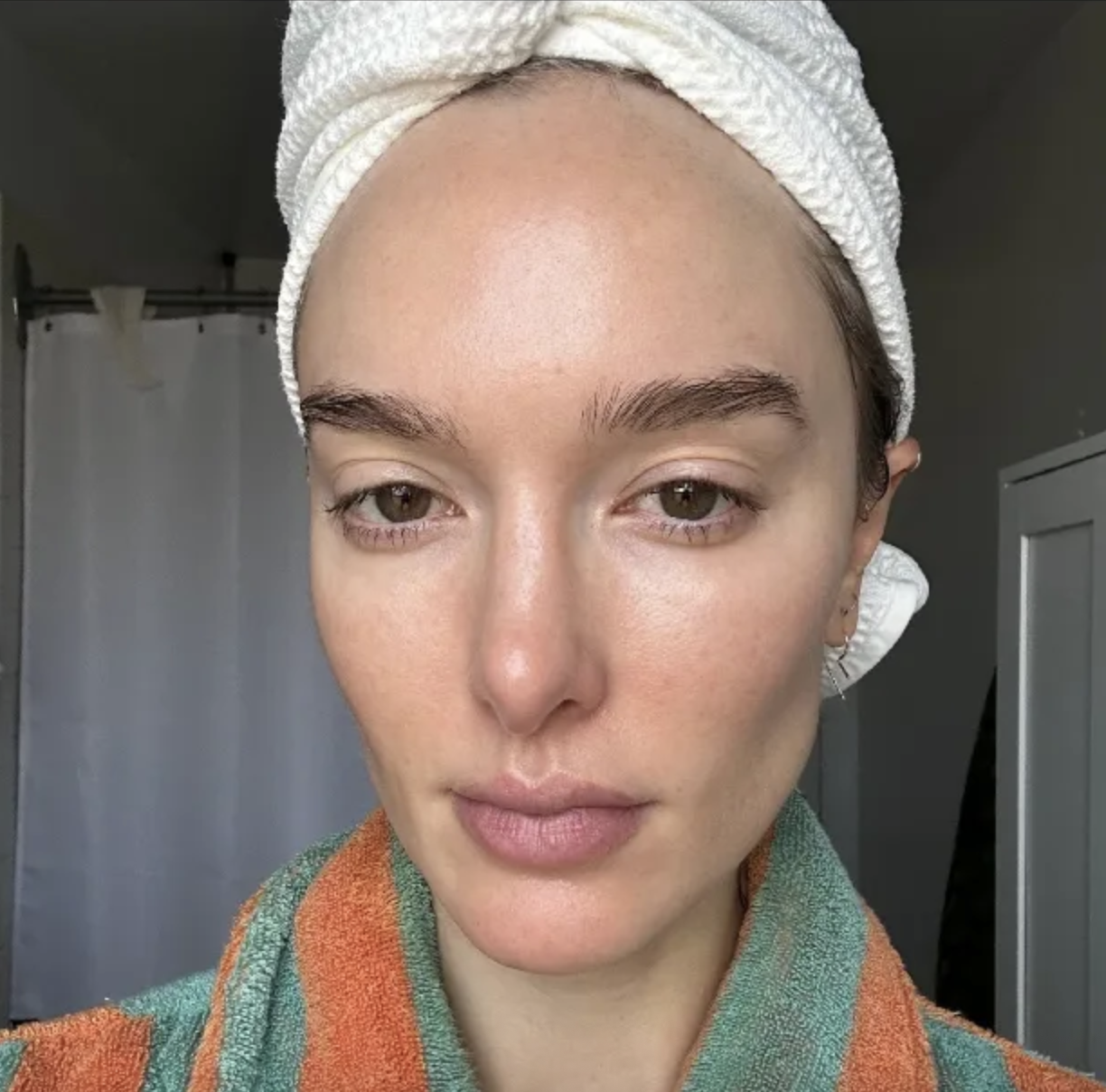 a woman in a green and orange robe and white head towel before the Ilia Skin Tint.