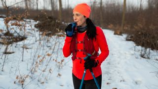 A woman hiking in the snow pauses for a drink from her hydration vest