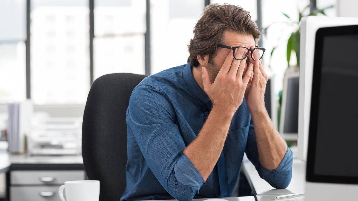 Man sitting at desk in office with his head in his hands