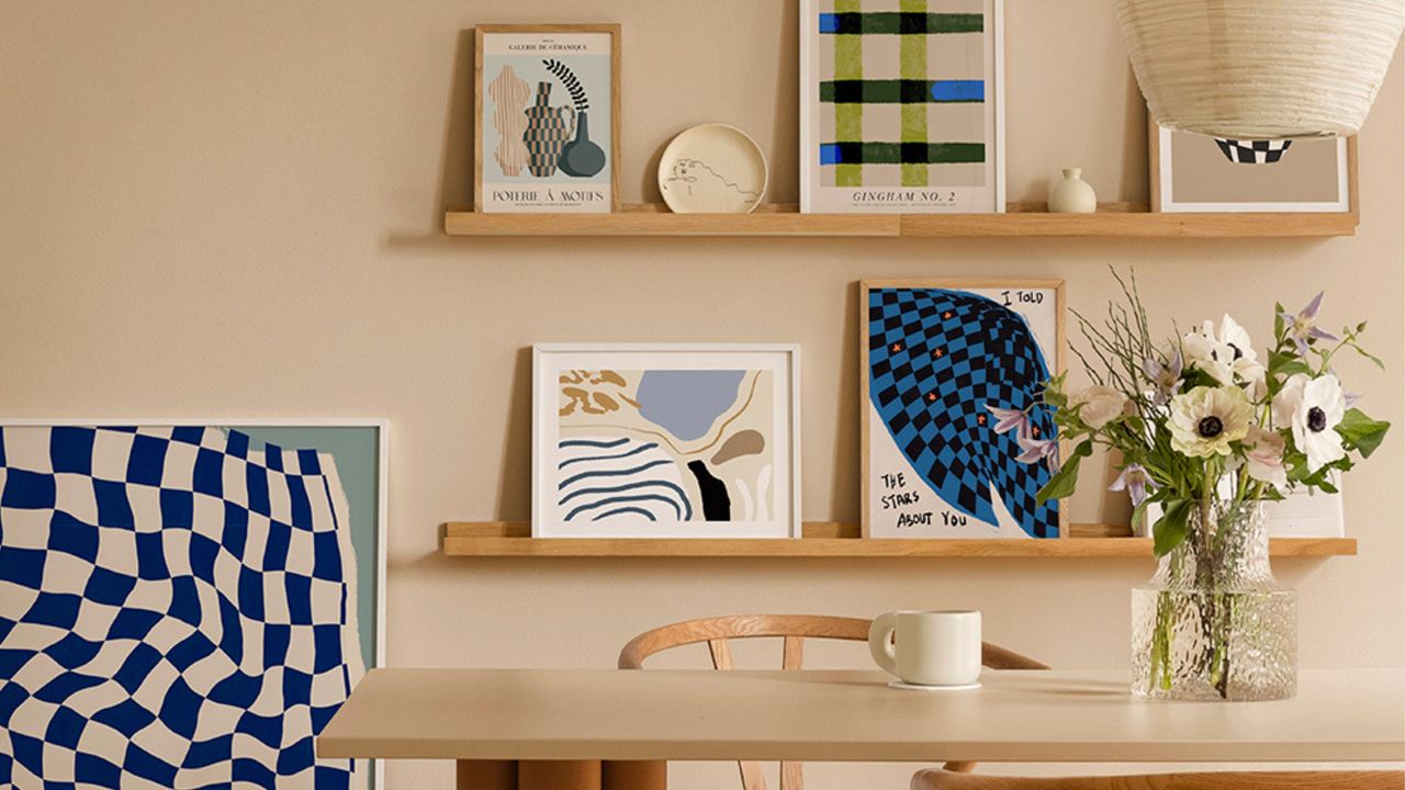 Dining room accent wall ideas are fab. Here is a light brown dining room with three wooden shelves with wall art prints on them, a light wooden dining set with a rectangular table and chairs and a cream pendant lamp