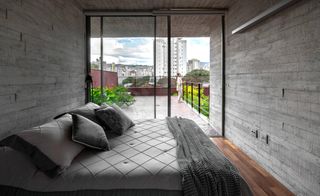Woman on terrace outside bedroom with concrete walls at Belo Horizonte home