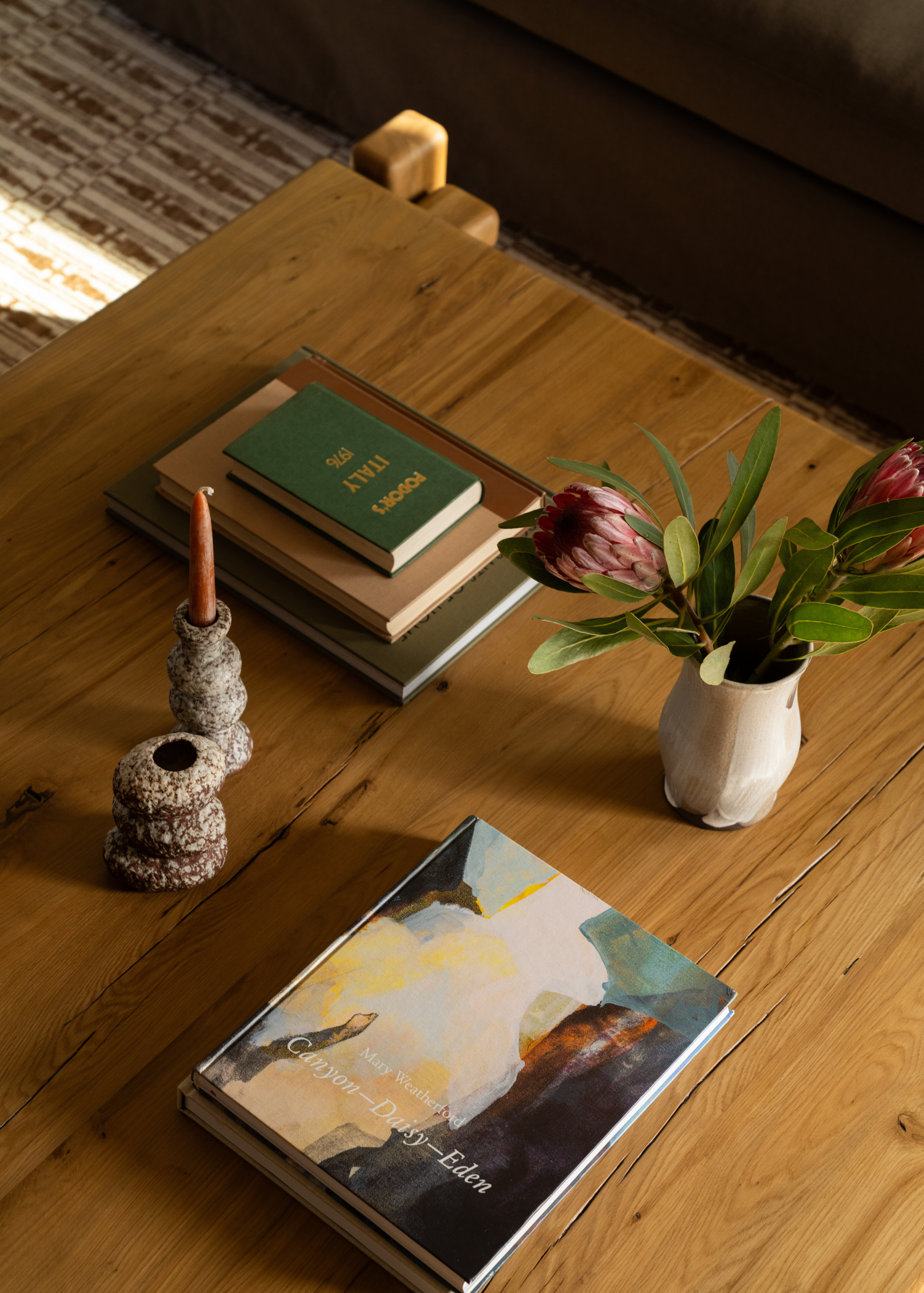 A wooen coffee table styled with books, candles and a small vase of fresh flowers