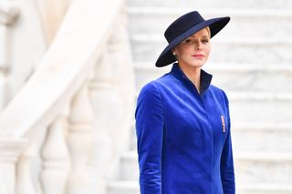 Princess Charlene wearing a blue dress and a striking black hat.