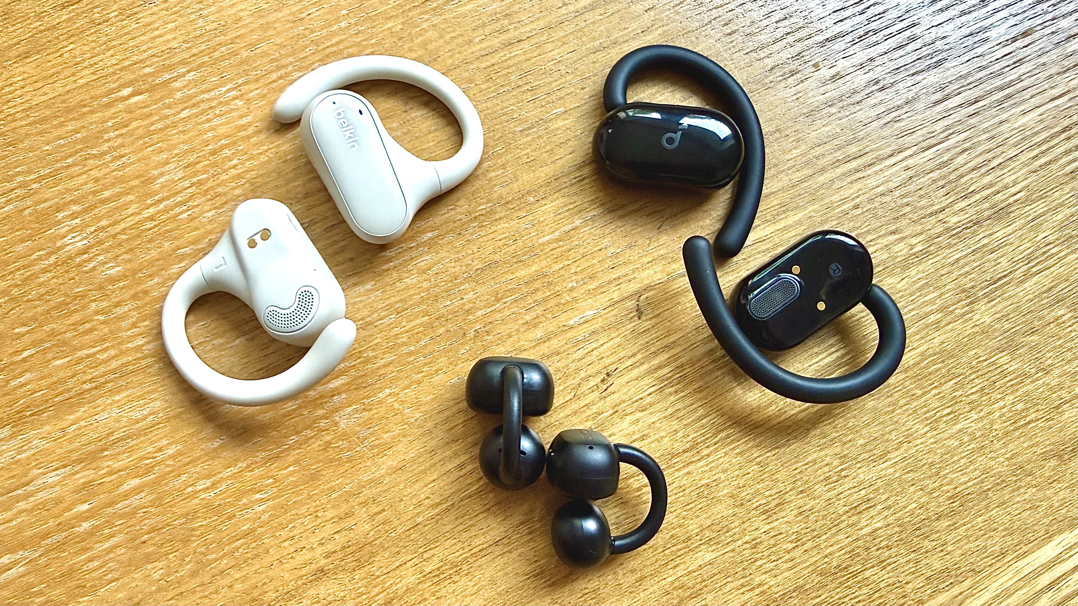 Three pairs of open earbuds on a wooden surface