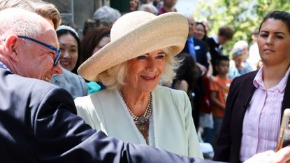 Queen Camilla wears a straw hat as she poses for a selfie with a royal fan during Australia tour