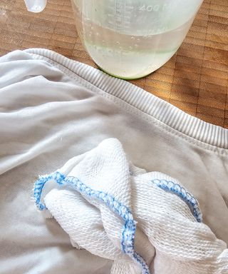 A white t-shirt with a white cloth on top of it, on a wooden chopping board with a plastic jug next to it